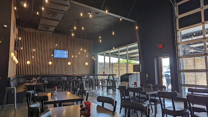 Modern commercial restaurant interior build-out showcasing custom wood slat wall features, acoustical ceiling elements, and decorative industrial lighting by Five Oak Construction